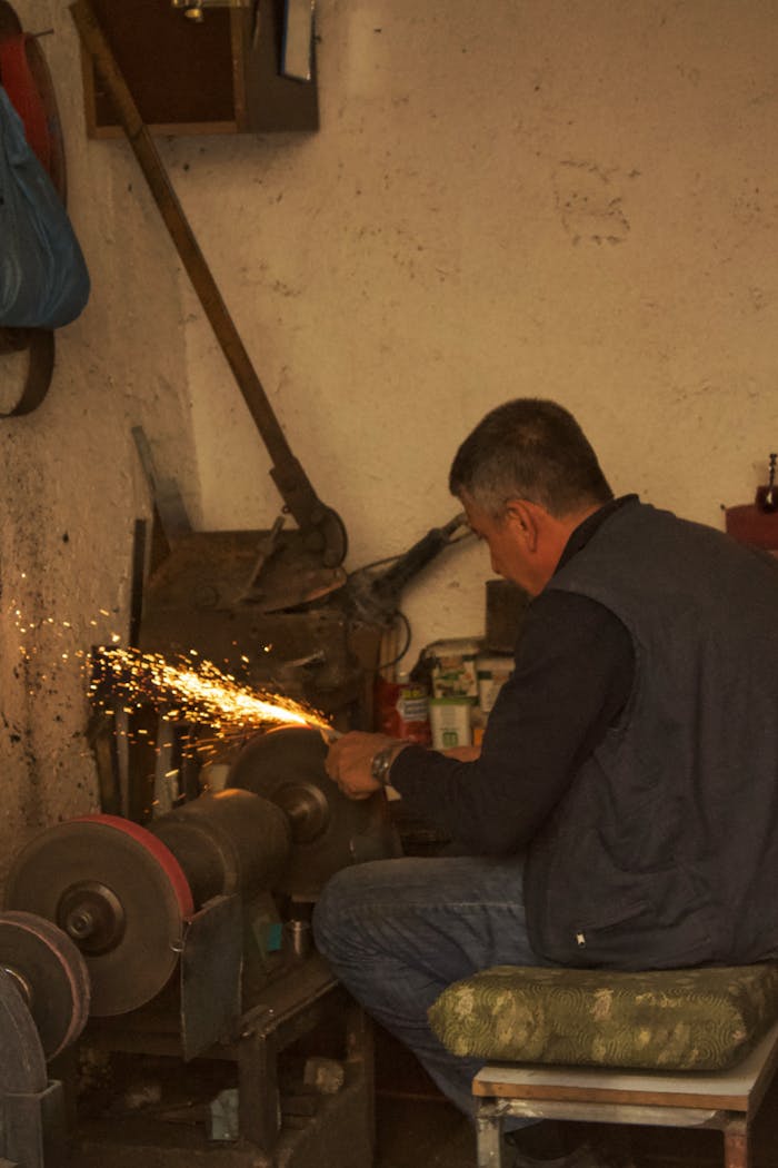 Man with short hair sharpening tools, creating sparks in a workshop setting.
