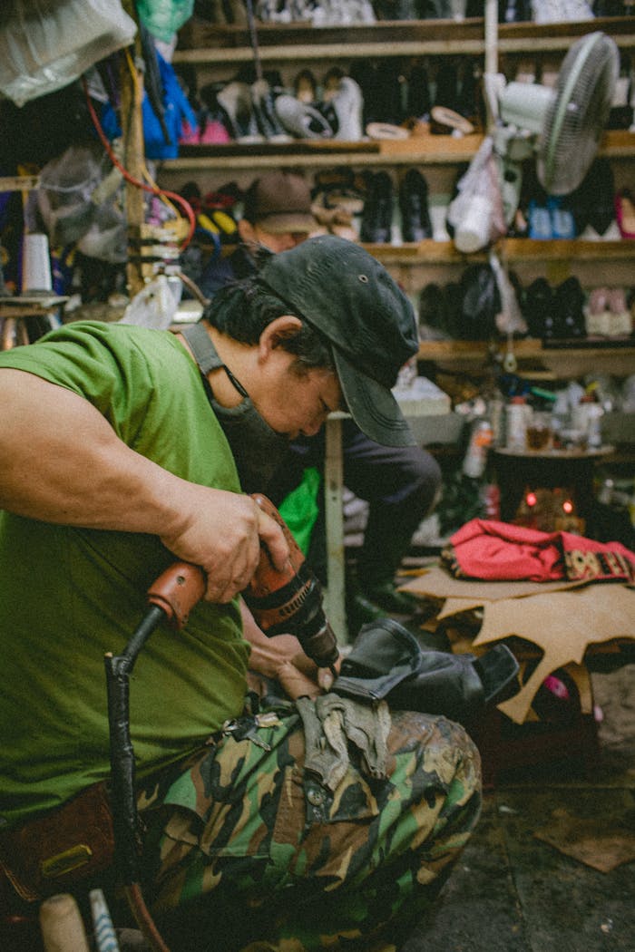 Shoemaker focusing on crafting in a cluttered workshop filled with tools and shoes.